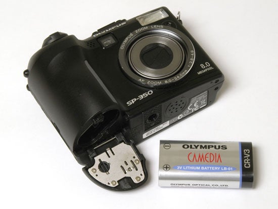 Olympus SP-350 digital camera displayed alongside its CRV3 lithium battery, with the battery compartment open.