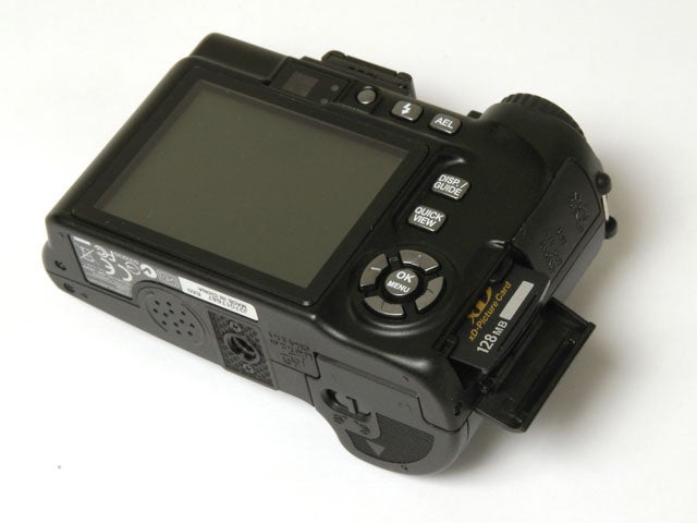 Olympus SP-350 digital camera with open memory card slot displaying the camera's rear controls and large LCD screen.