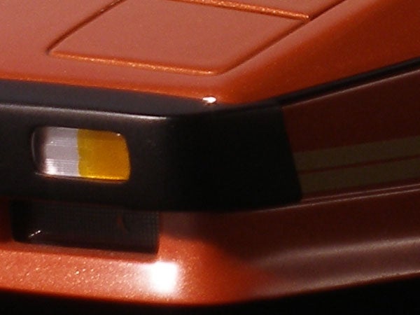 Close-up of a portion of a vintage orange Olympus SP-350 digital camera showing the flash and part of the lens barrel.