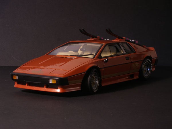 A metallic bronze toy model of a sports car with visible interior details, black trim, and mounted ski racks on a dark background.