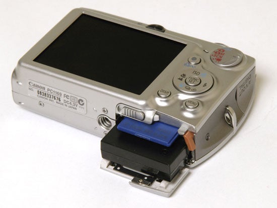 Canon Digital IXUS 750 camera lying on its back with the battery compartment open and the battery partially ejected.