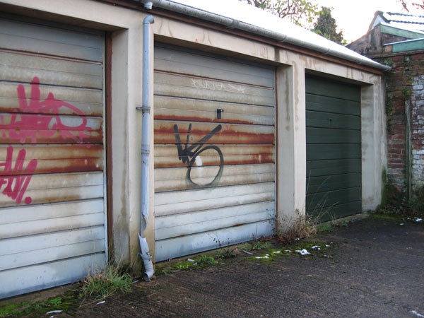 A photograph depicting three garage doors, with the central one featuring graffiti art, captured in natural daylight.