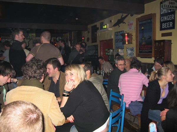 Photograph taken with a Canon Digital IXUS 750 camera capturing a lively scene inside a bar with multiple people engaged in conversations.
