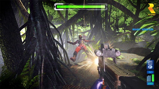 In-game screenshot from Perfect Dark Zero showing a character in a red suit jetpacking through a jungle environment with a player's first-person view of a gun aiming at the character. A health bar is visible at the top and the game's HUD displays ammo count and a minimap.