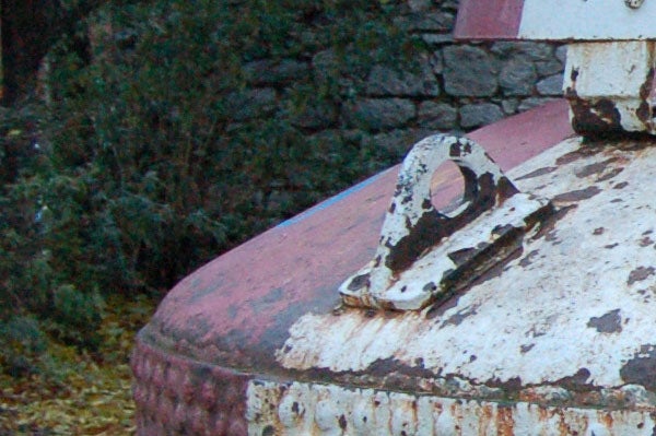 Close-up of a weathered and rusty metal surface with flaking white and red paint, possibly a detail of an old industrial object or equipment.
