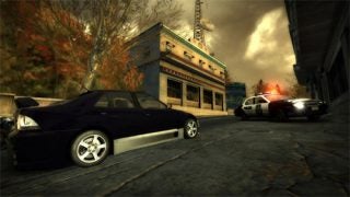 An in-game screenshot from Need for Speed: Most Wanted 2005 showing a black sports car in a street race with police cars in pursuit during what appears to be sunset or sunrise.