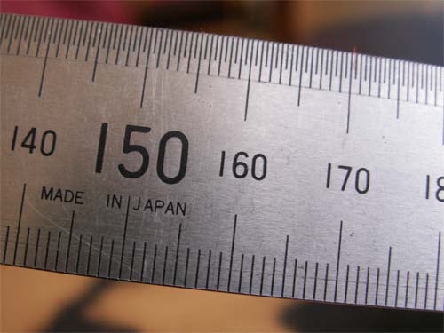 Close-up photo showing a precision scale ruler with measurement markings indicating the focal lengths between 140 and 180 millimeters, Made in Japan, possibly demonstrating the macro capabilities of the Konica Minolta Dimage Z6 camera.