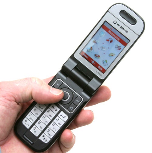 A hand holding a Toshiba TS803 - 3G Music Phone, shown in an open flip position revealing its screen and keypad.