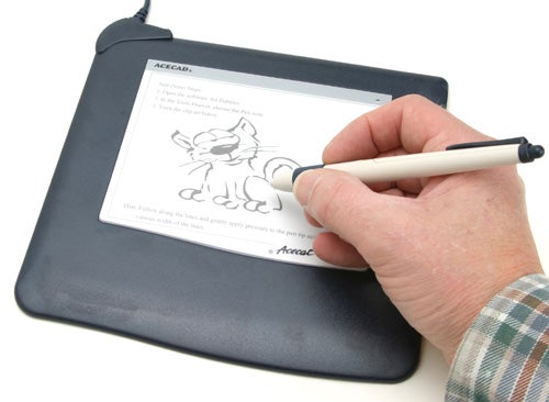A person's hand using a stylus on the Acecad Acecat Flair graphics tablet to draw a cartoon cat on the screen.