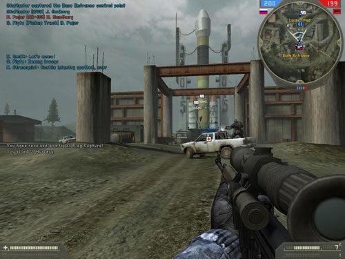 In-game screenshot of Battlefield 2: Special Forces showing a first-person view with a sniper rifle aiming towards a guarded facility entrance with a vehicle and multiple in-game characters. The heads-up display (HUD) presents the player's health, ammunition count, mini-map, and teammate communications.