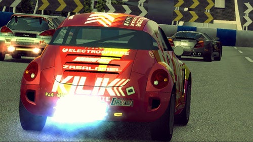 Red race car with various sponsor logos racing on a track in Ridge Racer 6 video game, closely followed by another race car.