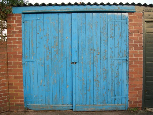 Blue wooden double doors with peeling paint on a small brick garage.