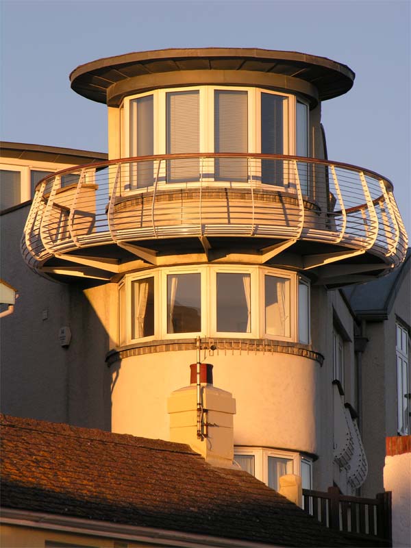 Photograph taken with a Nikon CoolPix 8800 featuring a close-up of a building with a rounded balcony and large windows during sunset, highlighting the camera's ability to capture warm lighting and architectural detail.