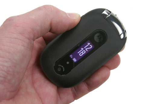 A hand holding a black Motorola PEBL phone with the flip-top closed and the external display showing the time.