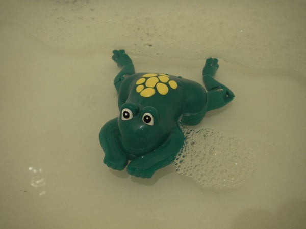 A green plastic toy dinosaur floating in clear water with bubbles around it.