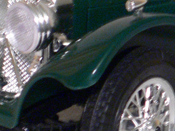 Close-up photograph demonstrating the detail and color rendition capabilities of the Panasonic Lumix DMC-LX1, showing the intricate parts of a green model car, including the wheel and headlight.
