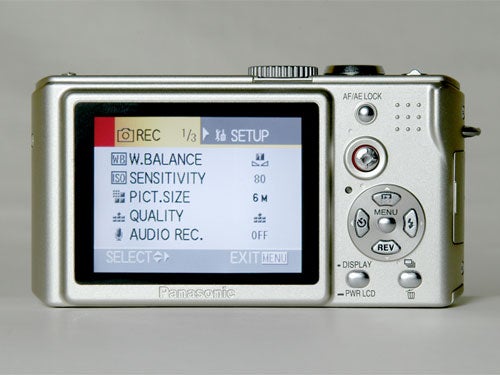 Panasonic Lumix DMC-LX1 camera on a white background, showing the setup menu on the LCD screen with options for white balance, ISO sensitivity, picture size, quality, and audio recording highlighted.