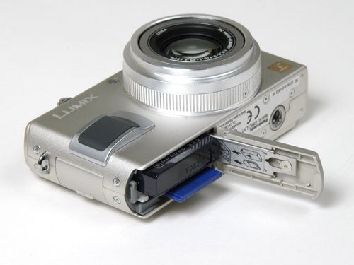 Panasonic Lumix DMC-LX1 digital camera with the battery compartment open, displaying the battery and memory card slot.