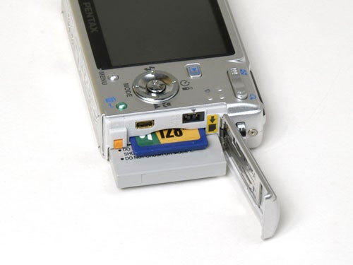 Pentax Optio S6 digital camera with open memory card slot and SD card partially inserted, displayed on a white background.