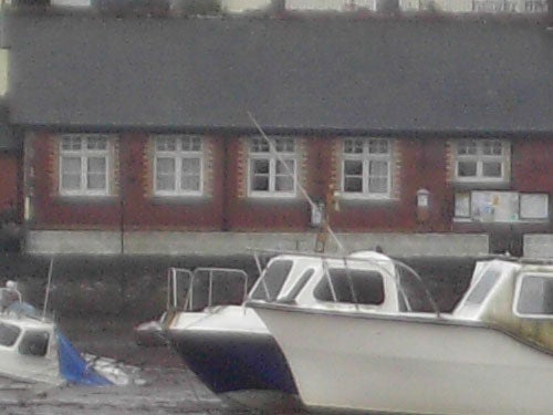 A low-resolution photo showcasing several boats moored on a body of water with a brick building in the background, potentially taken with an Acer CU-6530 to demonstrate image quality.