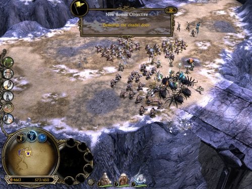 Screenshot from the video game 'Lord of the Rings: Battle for Middle Earth II' showing an in-game battle scene with various units clashing on a mountainous terrain, a new bonus objective indicating 'Destroy the citadel doors' at the top of the screen, and the game's user interface with minimap, resources, and unit controls visible.