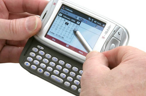 Hands holding a T-Mobile MDA Vario smartphone with the full QWERTY keyboard extended, using a stylus on the touch screen calendar application.