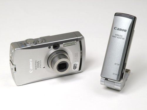 Canon IXUS digital camera alongside its wireless print adapter on a white background.