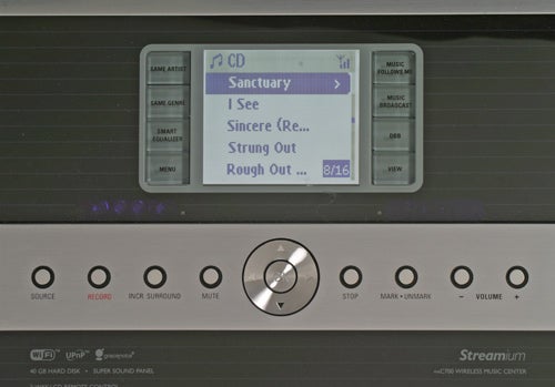 Close-up of a Philips WACS700/05 Wireless Music Station's control panel with display screen showing the CD function and track list, with buttons and the central dial below the display for various controls like source, record, function, and volume adjustment. The logo 'Streamium' is visible, indicating it's an active wireless music system.