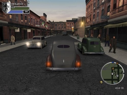 Screenshot from The Godfather video game showing a vintage car on a city street with pedestrians and other vehicles, with the in-game mini-map and currency displayed on the screen.