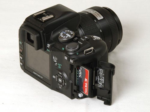 Olympus E-500 digital SLR camera with the memory card compartment open, showing a Compact Flash card inserted and a side-mounted lens attached.