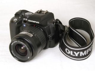 Olympus E-500 digital SLR camera with a standard zoom lens and attached neck strap on a white background.