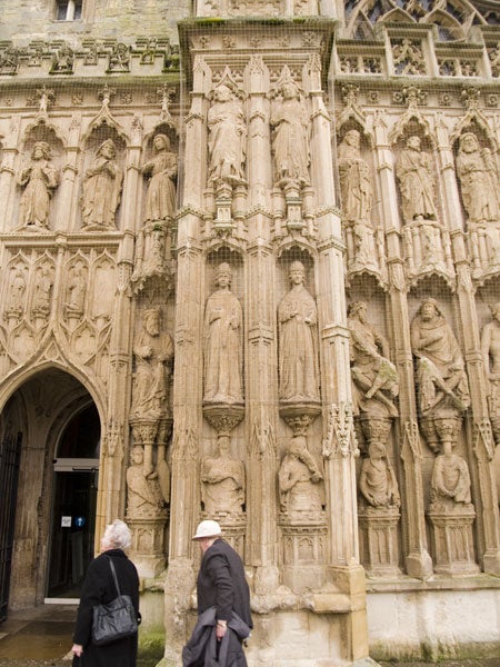 Photograph demonstrating the Olympus E-500 Digital SLR's clarity in capturing details of an ornate historic stone facade with sculpted figures, taken in overcast lighting conditions with two individuals walking by in the foreground.