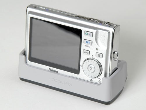 Nikon Coolpix S5 digital camera in silver color placed on a matching docking station with a clear view of the camera's large LCD screen and control buttons.