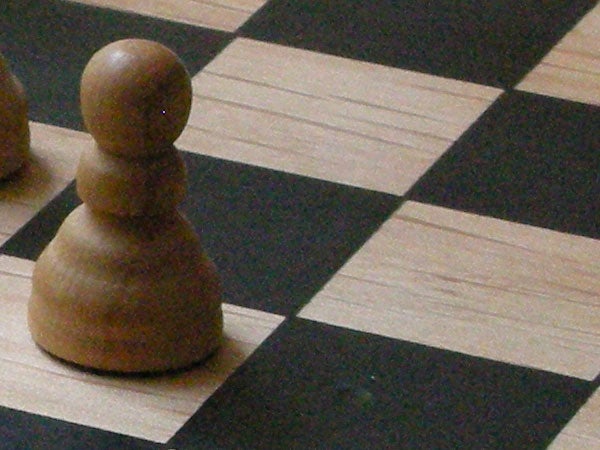 Close-up photograph of a wooden pawn on a chessboard showcasing shallow depth of field, possibly taken with a Nikon Coolpix S5 camera.
