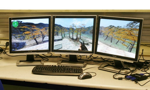 Three monitors set up side by side displaying an extended desktop image with a video game scene, with a keyboard and mouse in front, suggesting the use of the Matrox TripleHead2Go for a multi-display gaming setup.