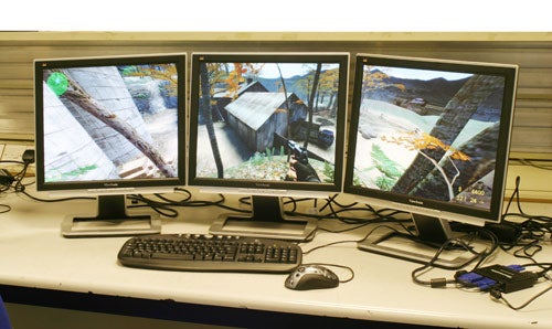 Three monitors displaying an extended desktop image with a video game scene, connected to a Matrox TripleHead2Go digital edition, with keyboard and mouse on a desk.