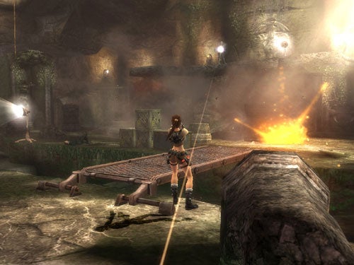 Screenshot of gameplay from Tomb Raider: Legend video game featuring the protagonist, Lara Croft, using a grappling hook to cross an ancient ruin environment with a visible explosion in the background.
