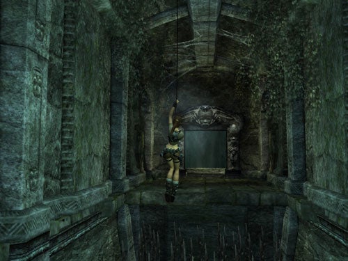 Screenshot from the video game Tomb Raider: Legend showing the main character, Lara Croft, using a grappling line to swing over a pit of spikes inside an ancient, dimly lit stone temple.