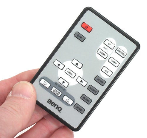 A person holding a BenQ projector remote control with clearly labeled buttons for power, menu navigation, and source switching.