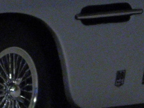 Photograph taken with a Nikon Coolpix P4 demonstrating image quality at high ISO settings, showing noise and detail on the surface of a toy car.