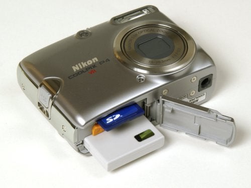 Nikon Coolpix P4 digital camera with the battery compartment open, showing the battery and SD memory card inserted.