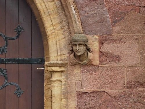 A stone sculpture of a human face embedded in a building wall next to a wooden door, possibly demonstrating the image quality from a Nikon Coolpix P4 camera.