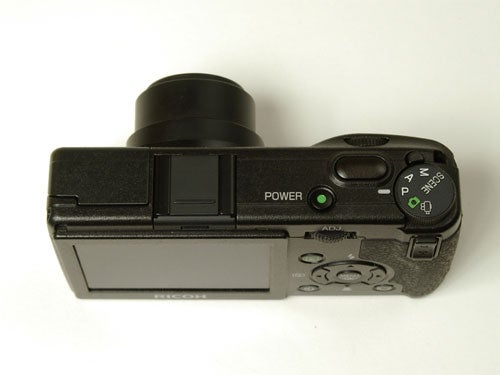 Ricoh GR Digital camera on a plain background, showing the back with LCD screen, control buttons, and a view of the power switch and mode dial.