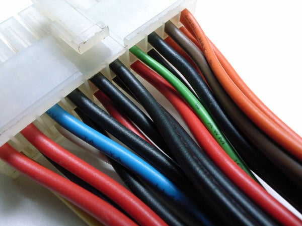 Close-up of multicolored electrical cables organized in a white connector block, showing wires in red, black, green, white, and blue.