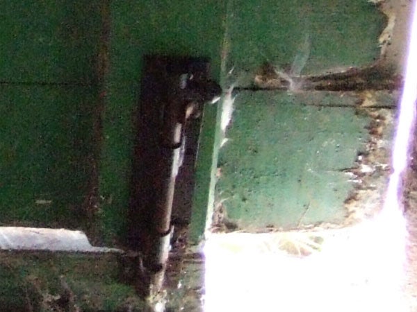 Close-up photo of a rusty metal bolt on a green painted door with visible cobwebs.