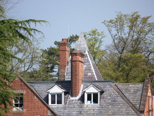Photograph of a brick house with a slate roof, featuring detailed brick chimneys and dormer windows, showcasing the zoom capabilities of the Kodak EasyShare V610 digital camera.