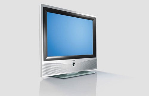 A Loewe Xelos A26 26-inch LCD TV on a reflective surface with a blank screen displaying a blue tint, a silver frame, central speaker grille, and placed on a clear glass stand.
