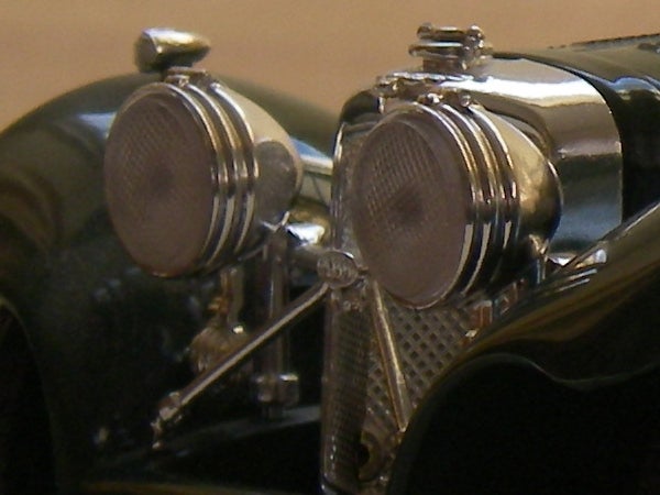 Close-up of a vintage car model showing intricate details like textured headlights, grille, and shiny chrome finishes.