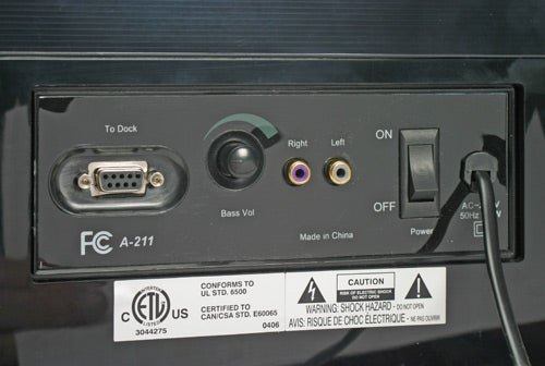 Back panel of an Acoustic Authority iRhythms A-211 speaker system, showing the To Dock connector, Bass Volume control, audio input jacks, power toggle switch, and various certification labels, against a black casing.