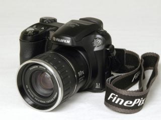 A Fujifilm FinePix S5600 digital camera with a 10x zoom lens and a neck strap displaying the FinePix brand name, photographed on a white background.